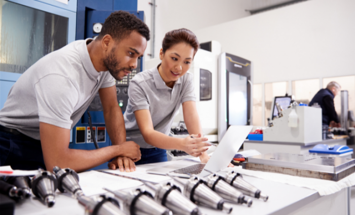 Two engineers working on a CAD programming software on a laptop